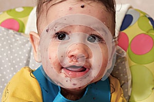 Portrait of little baby boy eating food. Baby with a spoon in feeding chair. Cute baby eating first meal