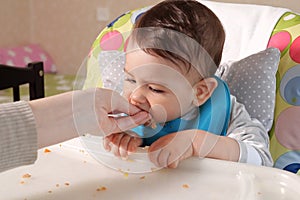 Portrait of little baby boy eating food. Baby with a spoon in feeding chair. Cute baby eating first meal