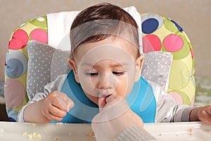 Portrait of little baby boy eating food. Baby with a spoon in feeding chair. Cute baby eating first meal