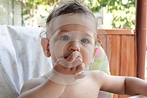 Portrait of little baby boy eating food. Baby with a spoon in feeding chair. Cute baby eating first meal