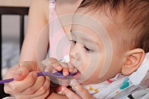 Portrait of little baby boy eating food. Baby with a spoon in feeding chair. Cute baby eating first meal