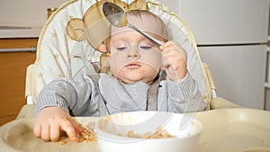 Portrait of little baby boy getting dirty and messy while eating porridge with spoon