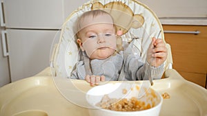 Portrait of little baby boy making mess while eating porridge by himself. Concept of parenting, healthy nutrition and baby feeding