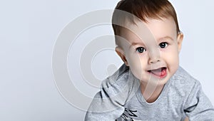 Portrait of little baby boy toddler in grey casual jumpsuit lying on floor, looking at camera and smiling over white background