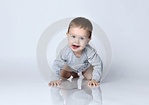 Portrait of little baby boy toddler in grey casual jumpsuit lying on floor, looking at camera and smiling over white background