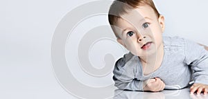 Portrait of little baby boy toddler in grey casual jumpsuit lying on floor and smiling over white wall background