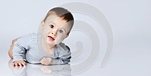 Portrait of little baby boy toddler in grey casual jumpsuit lying on floor and smiling over white wall background