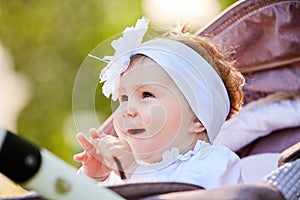 Portrait of the little baby girl sitting in a children`s carriage in summer day.