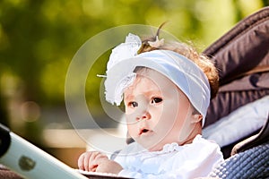 Portrait of the little baby girl sitting in a children`s carriage in summer day.