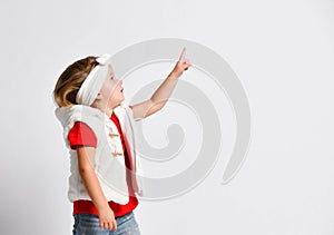 Portrait of little baby girl in white vest and red t-shirt pointing up at something on free copy space, showing on white