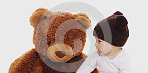 Portrait of little baby sitting on the floor with big teddy bear toy on white background