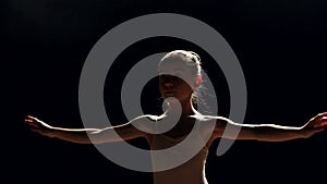 Portrait of a little ballerina girl on a black background on a stage.