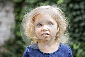 Portrait of a little beautiful European girl with curly blonde hair and blue eyes of 3 to 4 years in a classic blue color dress,