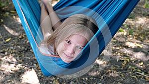 Portrait of a little blond caucasian girl lying in a blue hammock outdoors on a sunny day. Vacation for children, rest