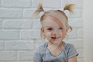 Portrait of little blond girl at the white brick wall,happy smiling toddler at home,sweet european child looking at