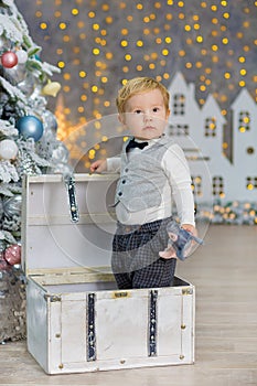 Portrait of little blonde boy sitting on roof in decorated studio and playing with Christmas presents and boxes. Decoration of