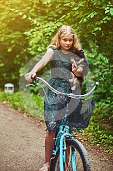 Portrait of a little blonde girl in a casual dress, holds cute spitz dog, in a park.