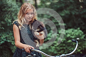 Portrait of a little blonde girl in a casual dress, holds cute spitz dog, in a park.