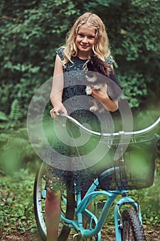 Portrait of a little blonde girl in a casual dress, holds cute spitz dog, in a park.