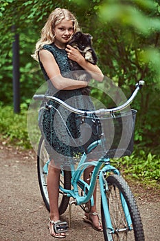 Portrait of a little blonde girl in a casual dress, holds cute spitz dog, in a park.