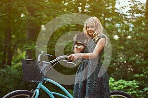 Portrait of a little blonde girl in a casual dress, holds cute spitz dog, in a park.