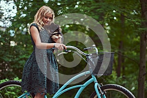 Portrait of a little blonde girl in a casual dress, holds cute spitz dog, in a park.