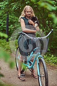 Portrait of a little blonde girl in a casual dress, holds cute spitz dog, in a park.