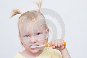 Portrait of a little blue-eyed blonde girl with pigtails on her head that brushes her teeth with a toothbrush, close-up