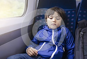 Portrait of little boy with bored face sitting alone on the train, Preschool kid traveling by train,  Child with unhappy face not