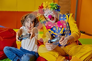 Portrait of little boy child and funny clown playing video games together photo