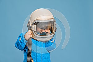 Portrait of little boy, child posing in astronaut costume, crying over blue studio background. Wiping tears