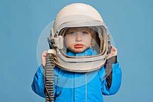 Portrait of little boy, child posing in astronaut costume over blue studio background. Crying baby