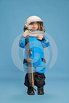 Portrait of little boy, child posing in astronaut costume over blue studio background. Emotional kid