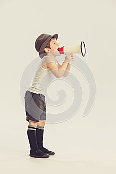 Portrait of little boy, child shouting in megaphone, playing isolated over grey studio background