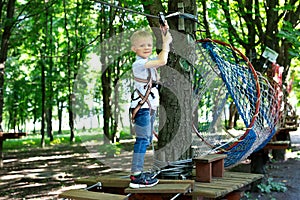 Portrait of a little boy in climbing gear in a rope park, holding a rope with a carbine.