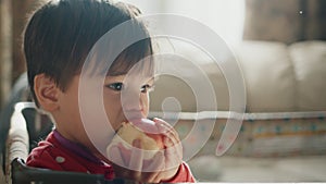 Portrait of a little boy, eating a big apple, standing in his crib