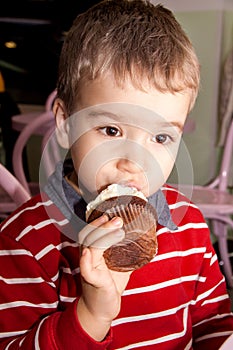 Portrait of a little boy eating tasty cocoa muffin with whipped topping photo