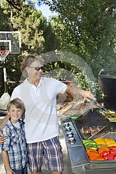 Portrait of a little boy with father barbecuing vegetable on barbecue grill in lawn photo