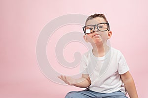 Portrait of a little boy in glasses, dressed in white t-shirt, pink background with copy space