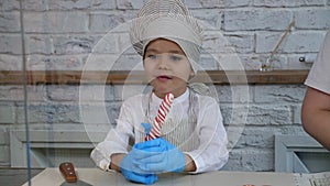 Portrait of a little boy in gloves and a cap with a lollipop in a candy store.