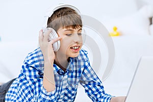 Portrait of little boy listening music from laptop through headphones while lying on hardwood floor