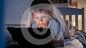 Portrait of little boy lying under blanket and using tablet computer. Children education, development, kids using gadgets secrecy