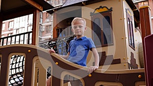 Portrait of a little boy on a modern playground, he stands on the bridge.