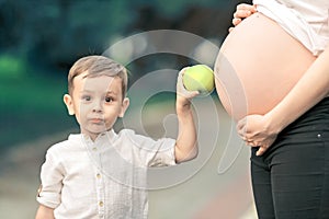 Portrait of a little boy next to a pregnant mother on a summer day in the park.