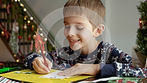 Portrait of little boy in pajamas writing a letter to Santa Claus with his wishes.