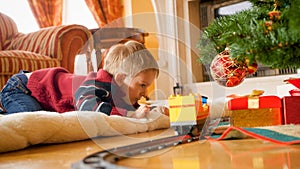 Portrait of little boy playing with toy train he got on Christmas from Santa Claus. Child receiving presents and toy on