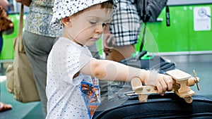 Portrait of little boy playing with wooden toy airplane in modern airport terminal