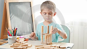 Portrait of little boy playing with wooden toy blocks and building tower from bricks. Concept of smart children and home