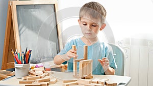 Portrait of little boy playing with wooden toy blocks and building tower from bricks. Concept of smart children and home