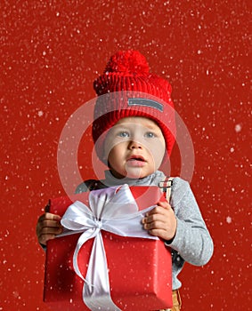Portrait of a little boy in a red hat with a pompon. holding a large gift box with a white bow.